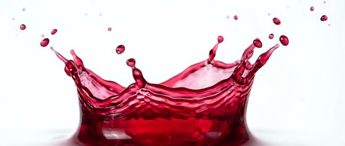 Dynamic red liquid splash with droplets frozen in motion against clean white background, perfect for beverage advertising and design projects.