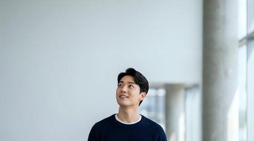 Young Asian male professional in black casual shirt gazing upward thoughtfully in modern office corridor with natural light, suitable for corporate, business, motivation, and lifestyle content.