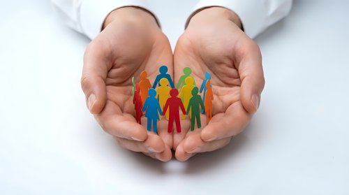 Protective hands cupping colorful paper cutout family figures representing care, support, community unity and social responsibility in healthcare concept.