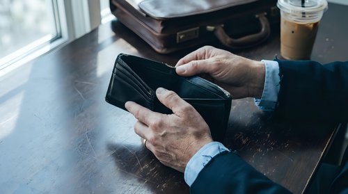 Senior businessman hands holding smartphone at office desk with briefcase and coffee cup nearby for mobile communication and work productivity.