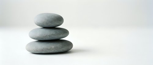 Three smooth gray zen stones stacked in balanced tower on white surface for meditation wellness spa relaxation mindfulness balance harmony concepts.
