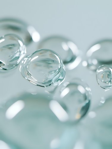 Transparent water drops or bubbles on light turquoise background with soft focus and bokeh effect, macro photography showing surface tension and reflection.