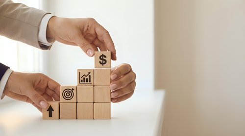 Business professional building wooden blocks with financial growth icons including dollar sign and chart symbols for strategic planning concepts.