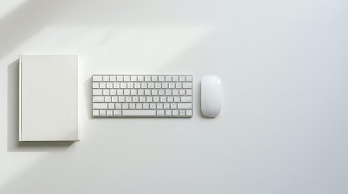 Minimalist white workspace with wireless keyboard, mouse and notebook on clean desk surface for modern office productivity and remote work setup.
