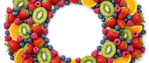 Fresh fruit wreath with strawberries, kiwi, blueberries and orange slices arranged in circle on white background for healthy eating and nutrition concepts.
