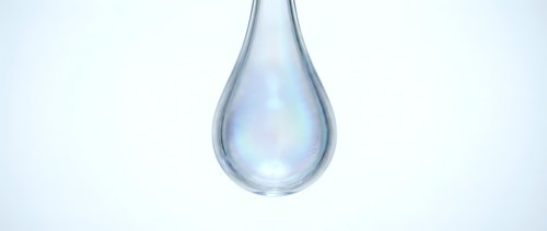 Clear water drop with iridescent rainbow reflections falling against clean white background for purity and freshness concepts in health and wellness designs.