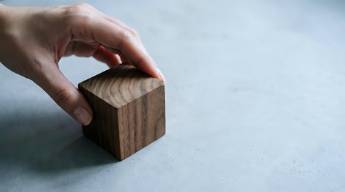 Hand placing wooden cube block on neutral surface for business strategy and building concepts in minimalist setting.
