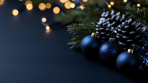 Navy blue Christmas ornaments and frosted pinecones arranged with evergreen branches against dark background with soft bokeh lights creating festive holiday mood.