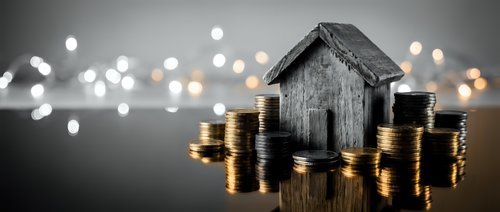 Wooden house model surrounded by stacks of golden coins with bokeh lights background representing real estate investment and property savings concept.