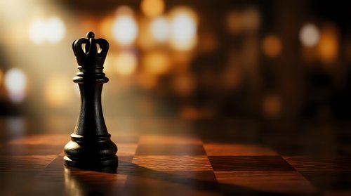 Black chess king piece standing on wooden chessboard with warm bokeh lights background for strategy and leadership concepts.