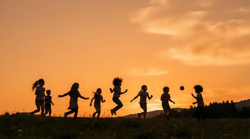 Silhouettes of diverse children holding hands and jumping together outdoors during golden hour sunset, representing friendship, unity, and outdoor play for family and community concepts.