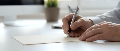 Close-up of male hands writing on blank white paper with pen at desk. Suitable for business, education, contract signing, note-taking, and office work concepts.