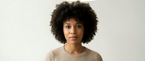 Young African American woman with natural curly afro hair wearing beige sweater against neutral background for lifestyle and fashion content.