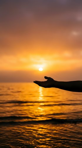 Human hand silhouette reaching toward golden sunset over ocean waves. Spiritual meditation concept for wellness and mindfulness content.
