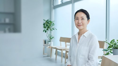 Professional Asian businesswoman in white shirt smiling confidently in modern bright office with plants and natural light for corporate presentations.