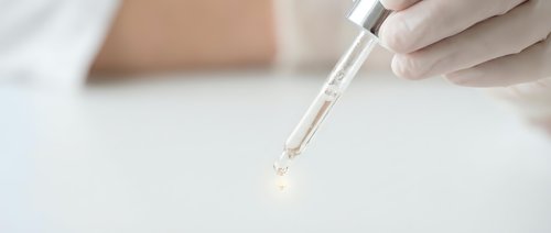 Medical professional in white gloves using glass pipette for precise liquid sample analysis in sterile laboratory environment for scientific research.