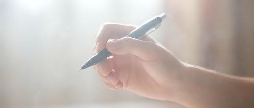 Close-up of female hand holding black pen in writing position against soft blurred background. Business professional ready to sign documents or take notes.