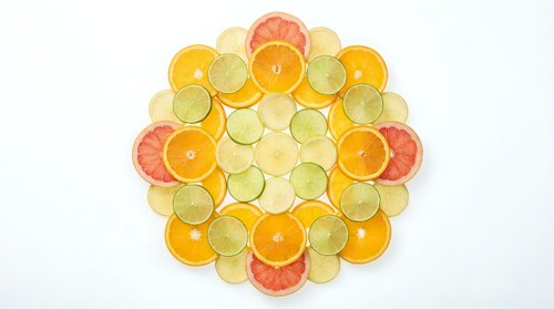Colorful citrus fruit slices arranged in circular mandala pattern on white background. Orange, lemon, lime and grapefruit creating vibrant geometric design.