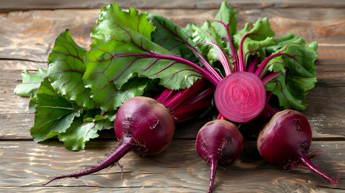 Fresh organic beetroots with green leaves and one cut in half showing vibrant pink flesh on rustic wooden background, natural light food photography.