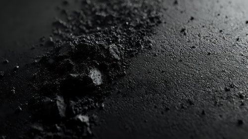 Dark textured surface with scattered powder and granular particles creating dramatic shadows and highlights against black background, macro photography for cosmetic products.