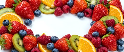 Fresh mixed berries and fruit slices arranged in heart shape on white background. Colorful assortment of strawberries, blueberries, raspberries, kiwi and orange.