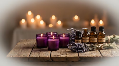 Spa aromatherapy setup with purple candles, essential oil bottles, dried lavender and warm ambient lighting on rustic wooden surface for relaxation.