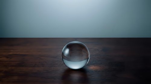 Clear glass crystal ball sphere sitting on dark wooden surface against blue gradient background for fortune telling and mystical concepts.