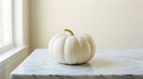 White pumpkin on marble surface near window with natural light for autumn seasonal decoration and harvest themed designs.