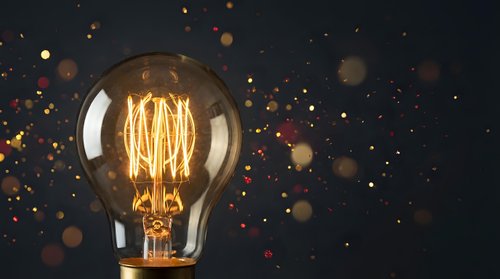 Vintage Edison light bulb with glowing filament against dark background with golden bokeh lights creating warm atmospheric lighting for creative projects.