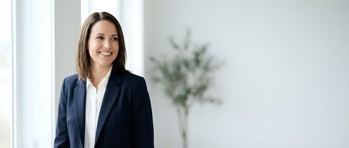 Professional businesswoman in navy suit smiling confidently in modern office environment with natural lighting and minimalist decor for corporate presentations.