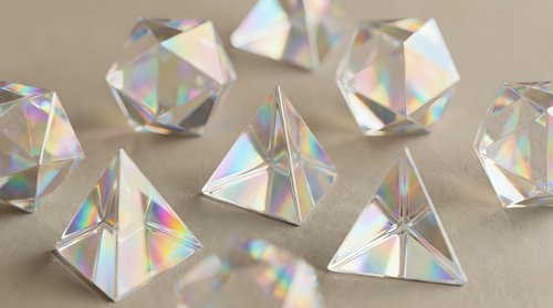 Crystal clear glass prisms and geometric shapes creating rainbow light reflections on neutral background for optical physics education and design projects.