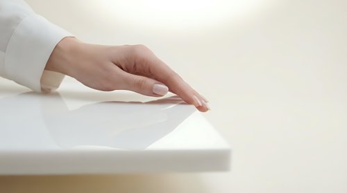 Woman's hand with manicured nails resting on white surface, wearing white long-sleeved shirt. Minimal, clean aesthetic suitable for business, wellness, and lifestyle design projects.