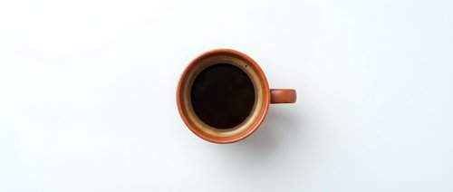 Orange ceramic coffee cup filled with black coffee viewed from above on white background for morning beverage and cafe design projects.