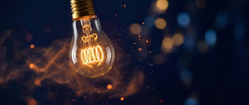 Glowing incandescent bulb with warm filament against dark background with bokeh particles, representing innovation, energy, and creative ideas for design projects.