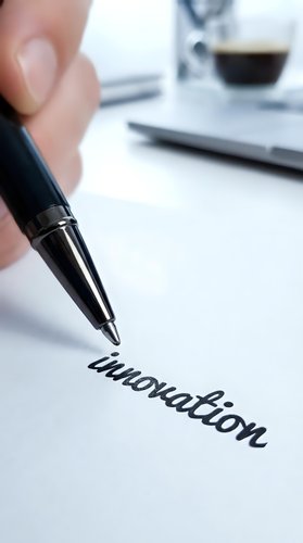 Close-up of hand holding black pen writing innovation on white paper at desk with coffee cup and notebook, suitable for business and creativity concepts.