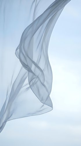 Flowing translucent blue fabric in motion against white background creating elegant waves and curves for fashion and textile design projects.