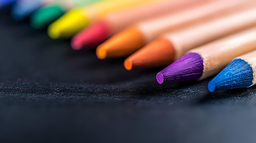 Vibrant colored pencils arranged in diagonal line on dark background with selective focus on purple and blue tips, creating artistic composition for education and creativity.