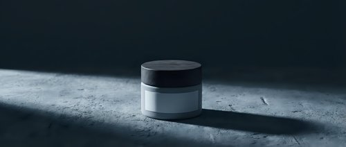 Luxury cosmetic jar with black cap on textured concrete surface with dramatic lighting and shadows for skincare product packaging design.