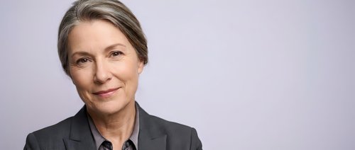 Mature woman with blonde hair wearing dark blazer against neutral background, suitable for corporate, business, and professional portraits.