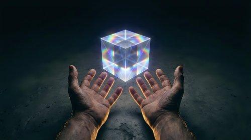 Hands reaching toward glowing holographic cube with rainbow light effects floating above palms against dark background for technology and innovation concepts.