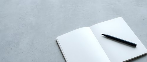 Open notebook with blank pages and black pen on gray textured surface, ready for writing, planning, or note-taking.