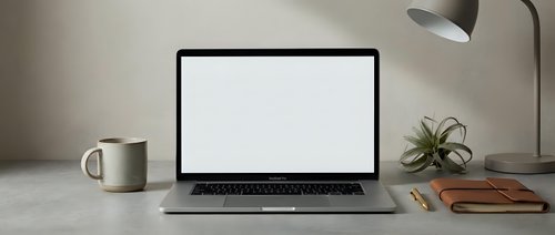 Modern workspace with open laptop displaying blank white screen on marble desk with coffee mug, plant, and lamp for productivity and business mockup designs.