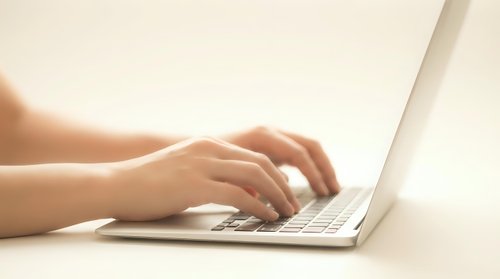 Female hands typing on modern laptop computer keyboard in bright natural light for remote work and digital productivity.