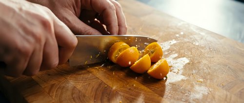 Person with knife slicing golden yellow bell pepper on wooden cutting board with flour dusting, food preparation for cooking and culinary use.