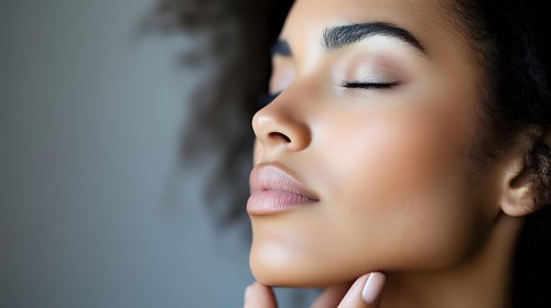 Close up profile portrait of young African American woman with natural curly hair, closed eyes, and serene expression showing wellness and beauty skincare concept.