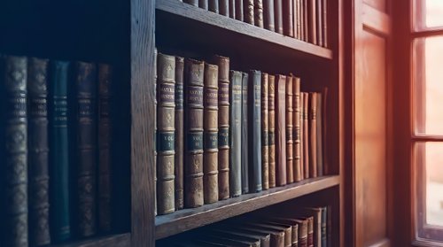 Vintage leather-bound books arranged on wooden library shelves with warm sunlight streaming through window creating atmospheric reading environment.