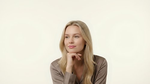 Professional blonde businesswoman in brown blazer posing thoughtfully with hand under chin on neutral background for corporate marketing materials.
