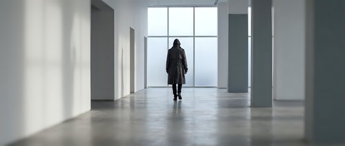 Woman in dark coat walking through modern empty corridor with large windows and concrete floor, suitable for corporate and architectural concepts.
