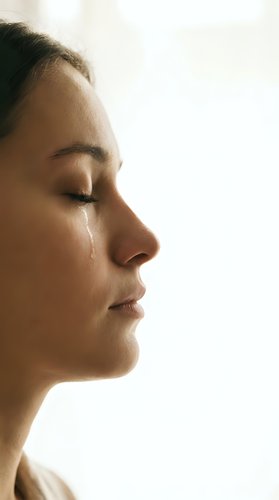 Young woman with closed eyes and tear on cheek in profile view showing emotional moment with soft natural lighting for mental health concepts.