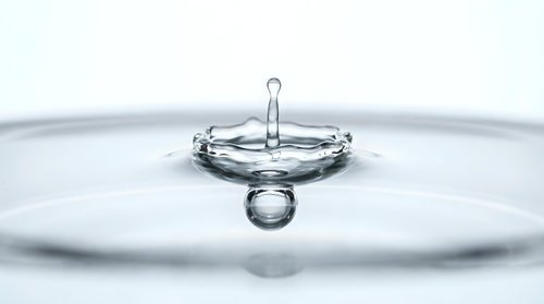 Water drop splash captured in macro with crown formation and ripples on light background, showcasing liquid motion and purity.